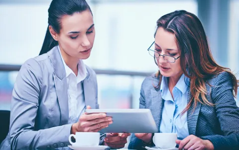 A couple of women looking at a tablet, representing collaboration and modern business intelligence through BW modernization.