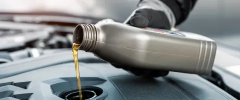 A person pouring engine oil into a car, representing automotive service operations and efficiency improvements enabled by SAP Datasphere.