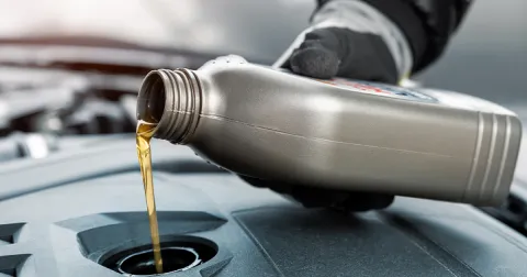 A person pouring engine oil into a car, representing automotive service operations and efficiency improvements enabled by SAP Datasphere.