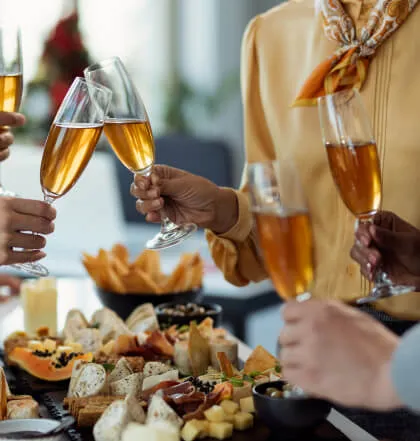 A group of people toasting with champagne glasses over a table filled with various appetizers and finger foods