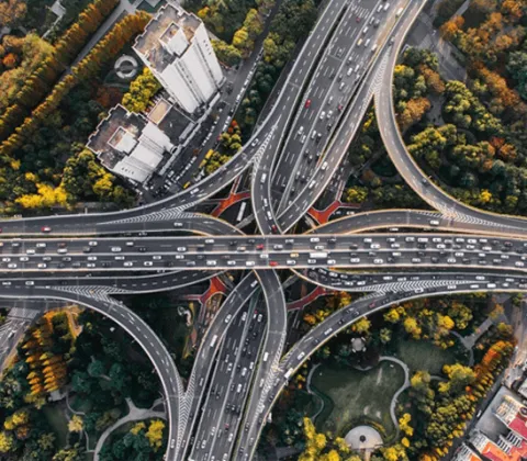 Aerial photograph of a large, multi-level highway interchange surrounded by green and yellow foliage and buildings. 