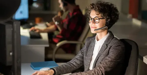 A customer support professional sitting in an office chair at a desk, working on a computer, focused on assisting customers through a support dashboard
